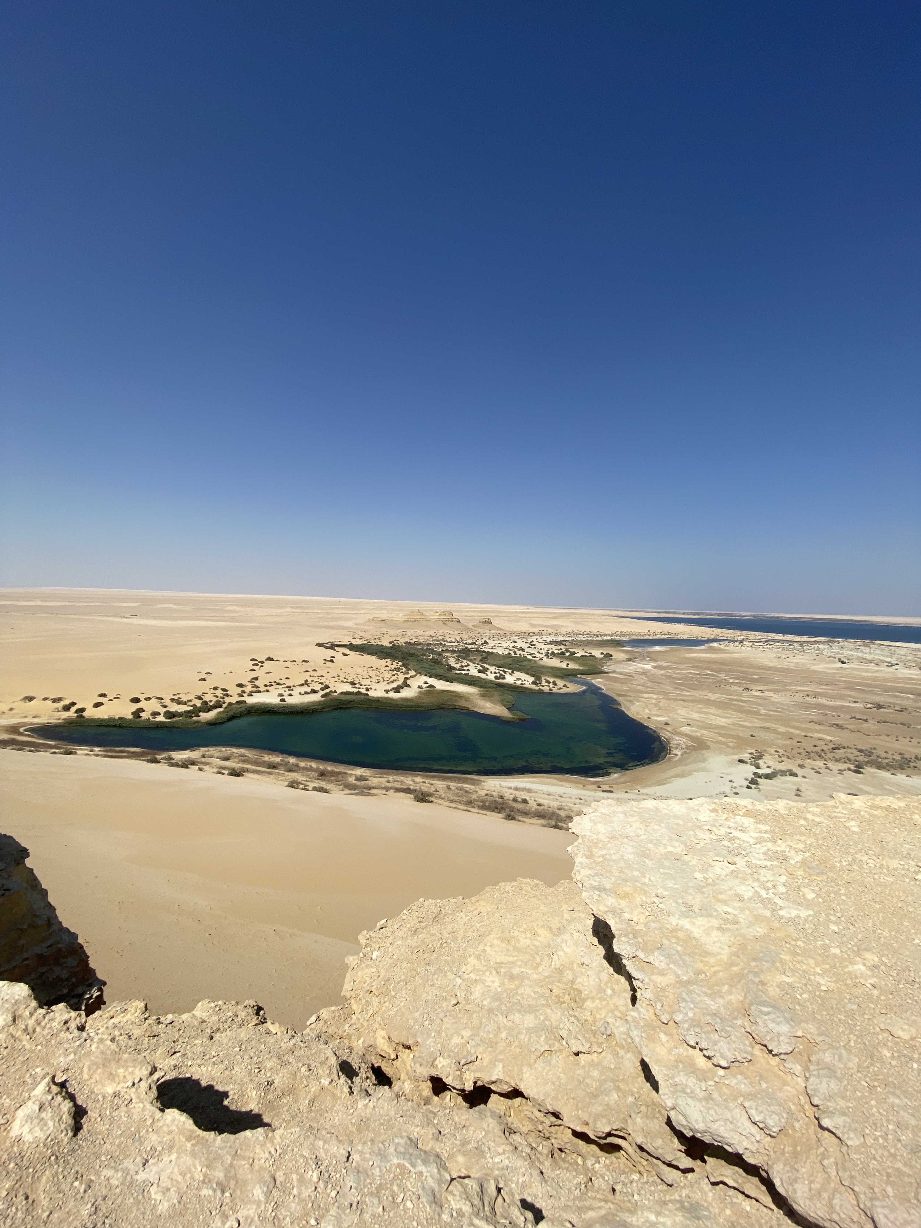 A high-angle view of a bright blue lake surrounded by the golden desert sands of Faiyum