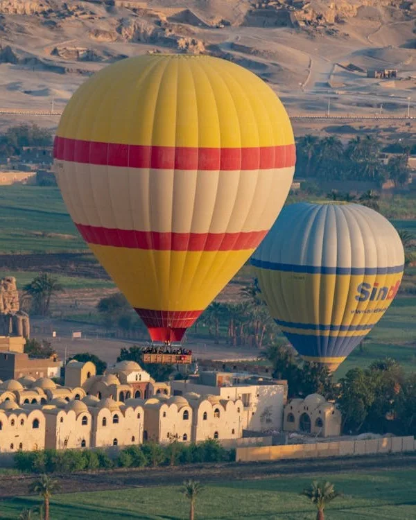 Deux grands ballons à air chaud flottent au-dessus d'un village près des collines désertiques de Louxor
